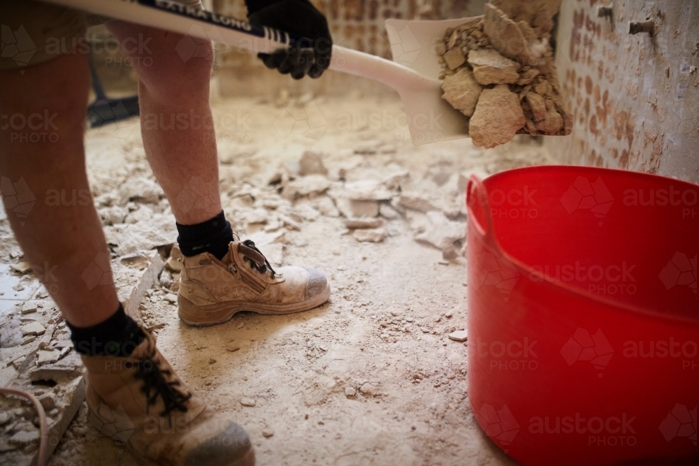 Tradesman shovelling debris into a bucket in a construction zone - Australian Stock Image