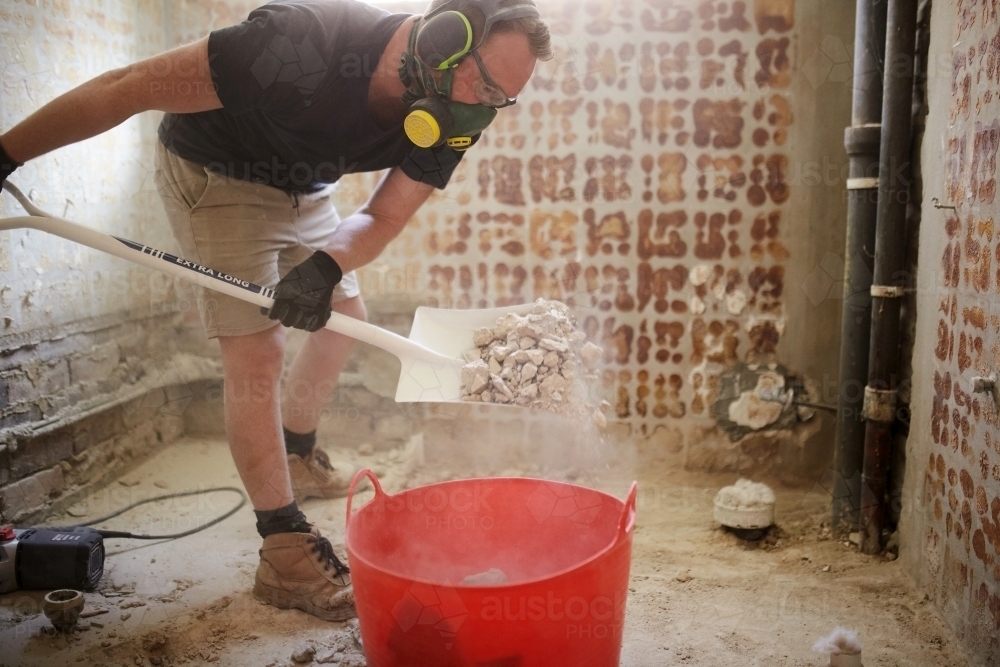 Tradesman shovelling debris into a bucket in a construction zone - Australian Stock Image