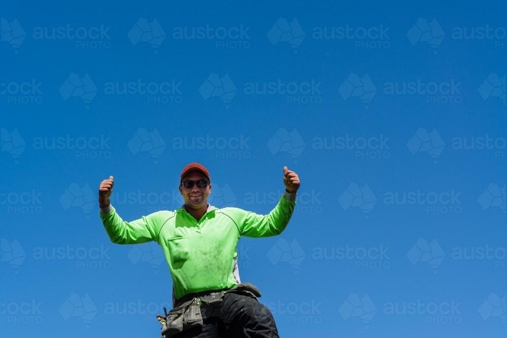 tradie doing thumbs up, in hi vis shirt, against blue sky - Australian Stock Image