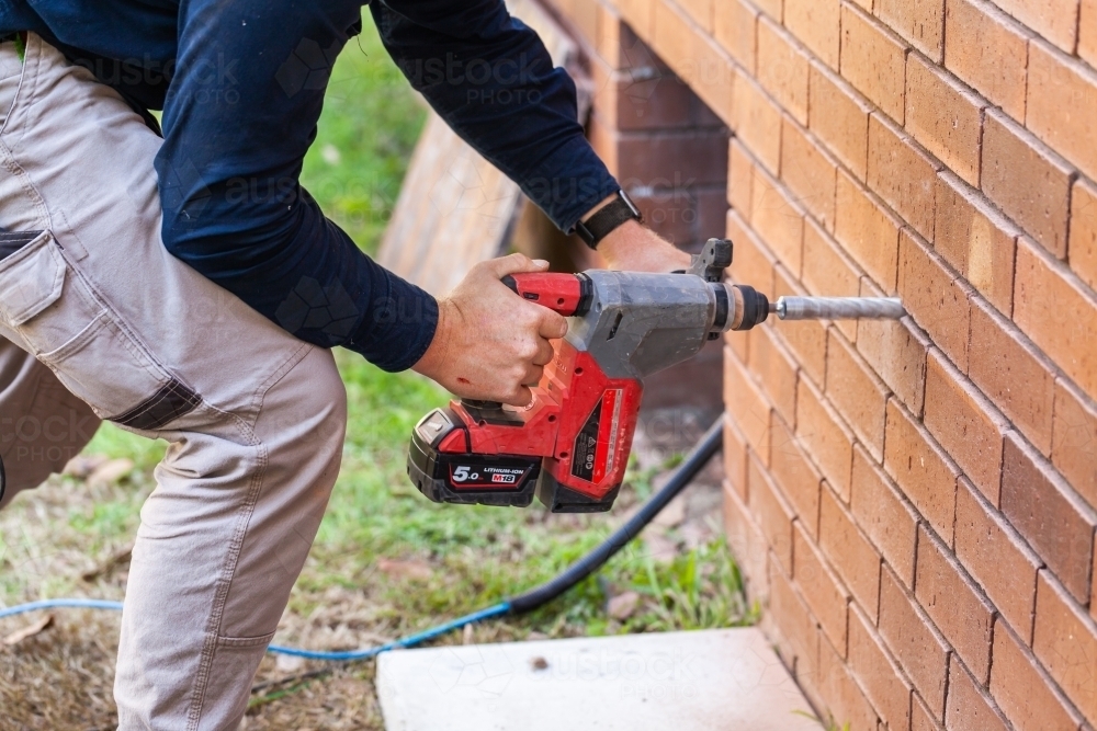 Tradie drilling hole in wall of house - Australian Stock Image