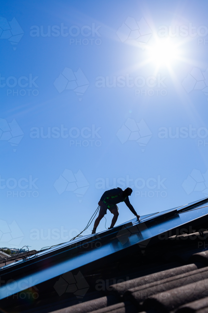 Tradie man laying solar panel on roof under blue sky during solar power system installation job - Australian Stock Image