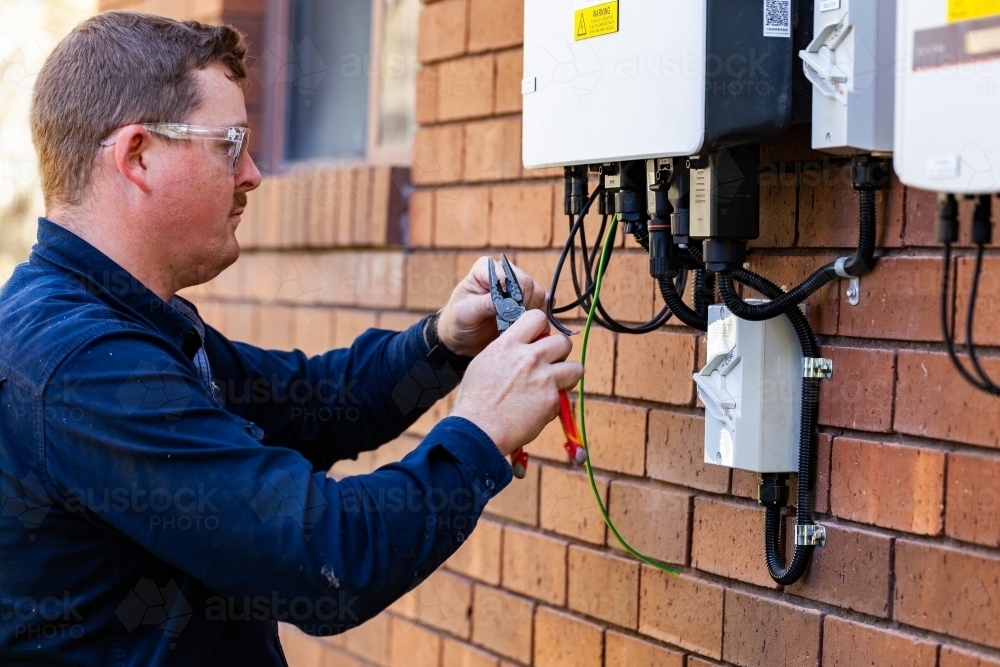 Tradie working as an electrician wiring a solar power control box beside house - Australian Stock Image