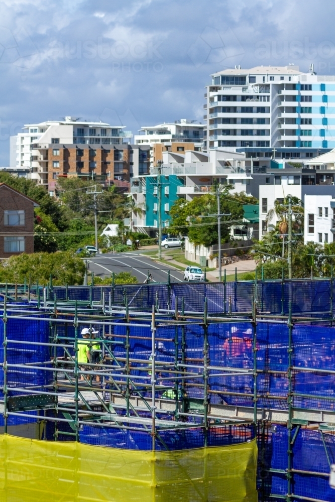 Tradies behind safety mesh and scaffold of new building construction site. - Australian Stock Image