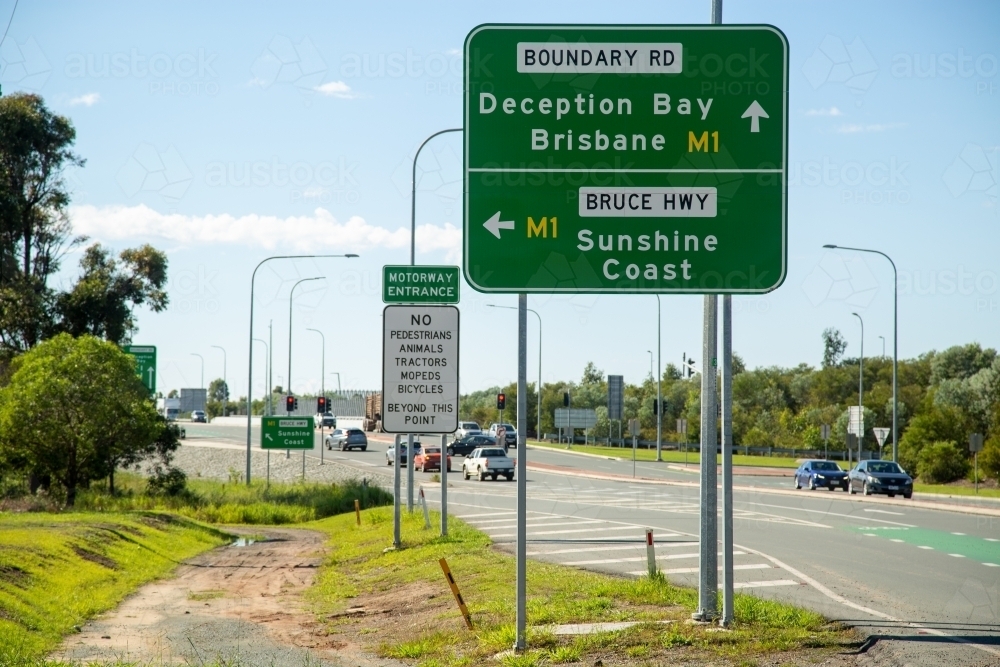 Traffic driving at intersection with signs to Brisbane, Sunshine Coast, and Deception Bay. - Australian Stock Image