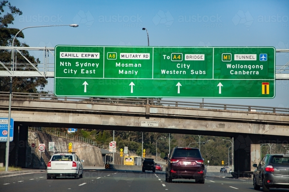 Traffic driving under bridge with signs to Sydney city east, city western suburbs, wollongong - Australian Stock Image