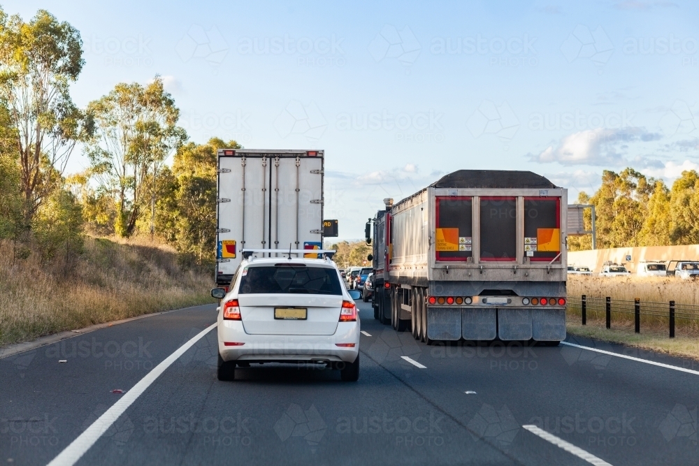 Travelling down Sydney bypass highway road behind car and truck on sunlit afternoon - Australian Stock Image