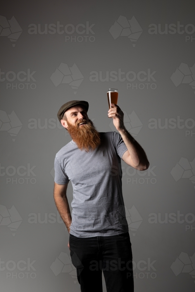 Trendy guy holding a glass of beer, relaxed and happy - Australian Stock Image