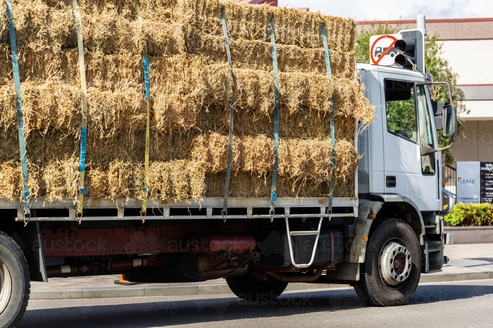 Truck full of hay bales driving down street of town - Australian Stock Image