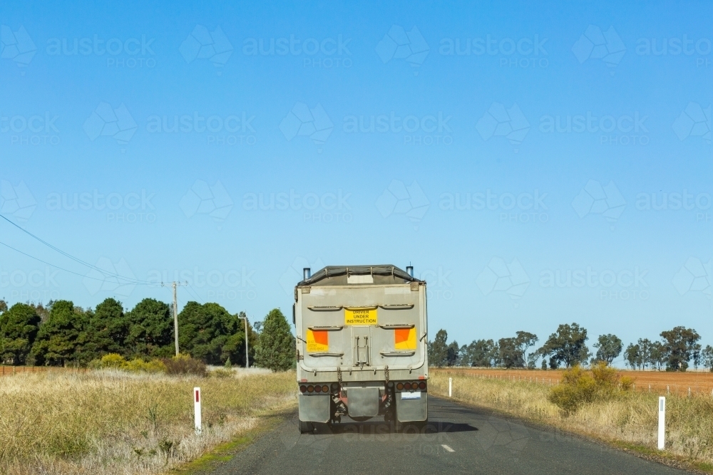 Truck with driver under instruction sign on back driving on remote rural road - Australian Stock Image