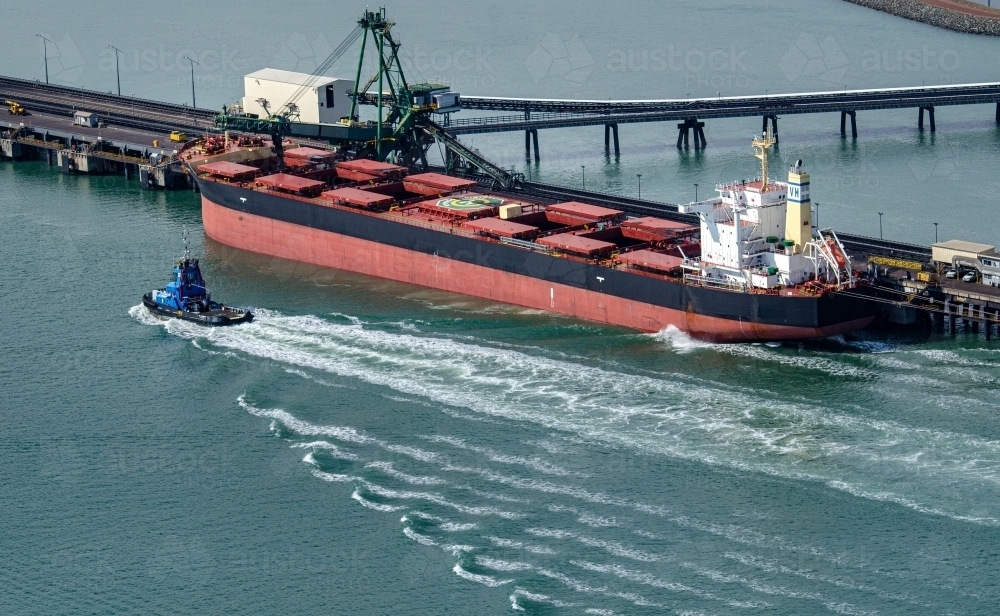 Tug boat passing by a coat ship and creating wash lines in the water - Australian Stock Image