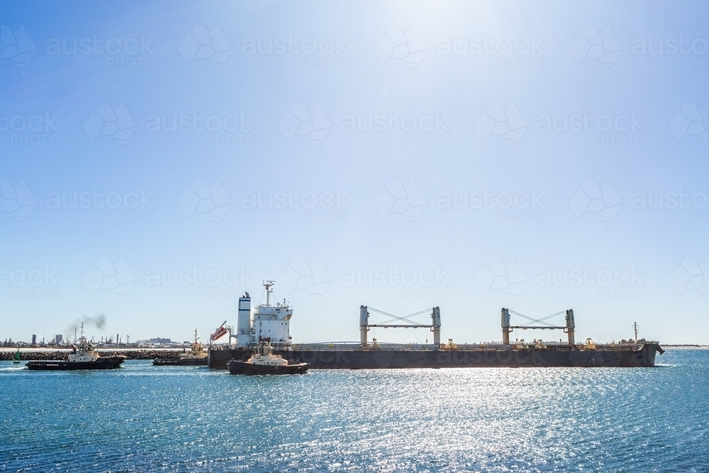 Tug boats assisting ship leave port of Newcastle on sunlit day - Australian Stock Image