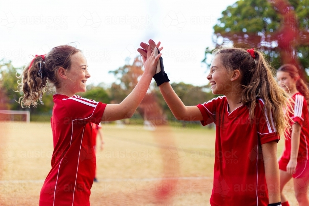 Tween female soccer players high-five in front of the goal net - Australian Stock Image