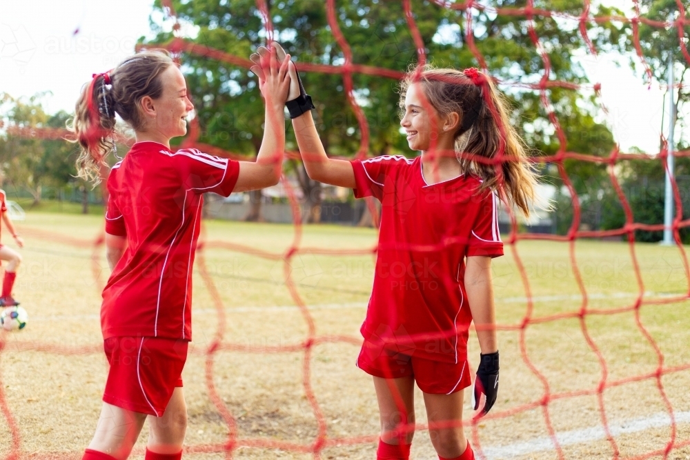 Tween female soccer players high-five in front of the goal net - Australian Stock Image