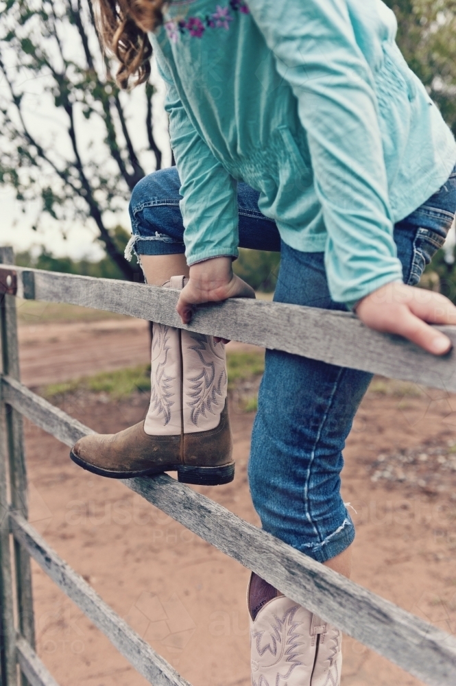 Tween girl climbing a timber fence on a rural property - Australian Stock Image