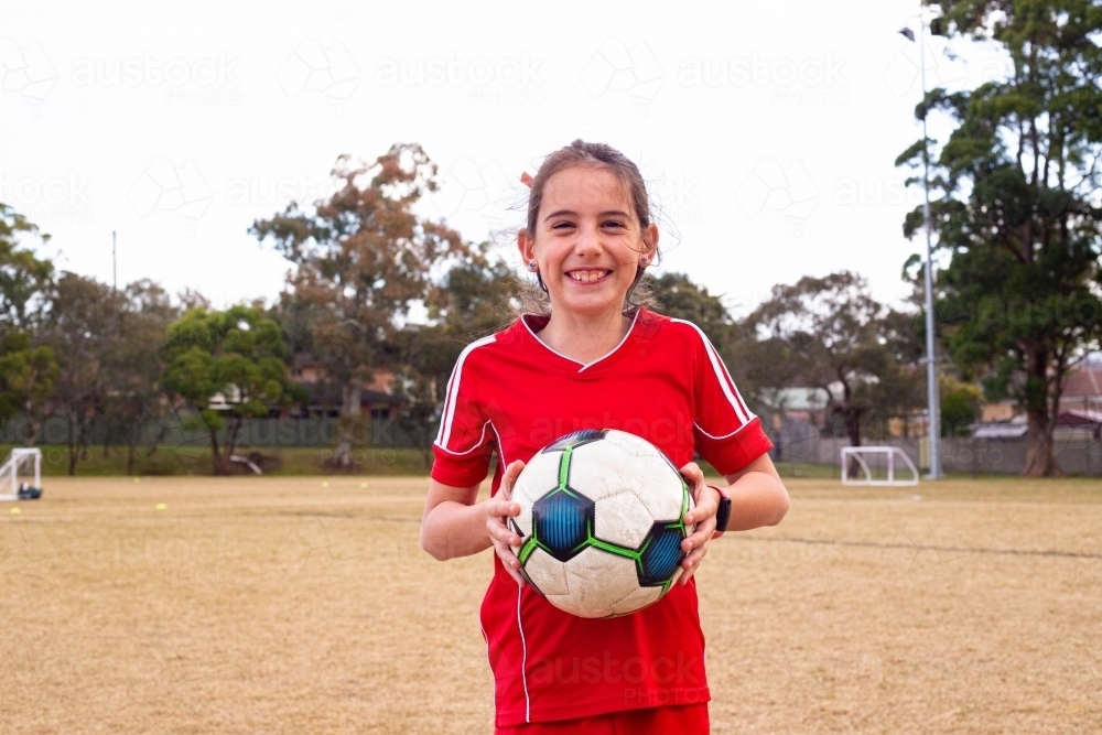 Tween girl in a red soccer uniform holding a ball - Australian Stock Image