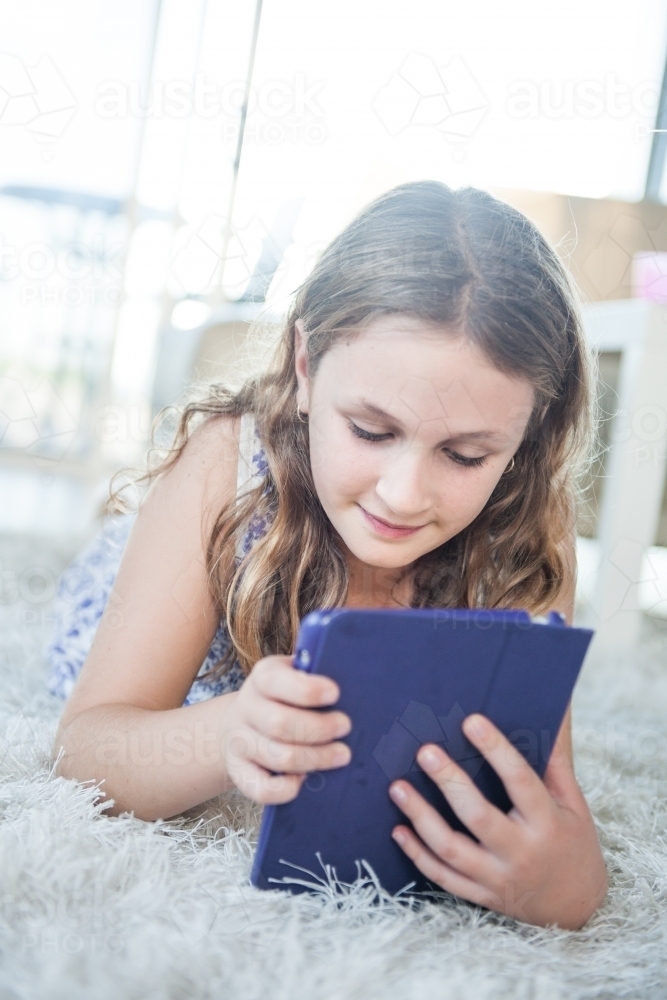 Tween girl using iPad whilst lying the floor on a white rug - Australian Stock Image