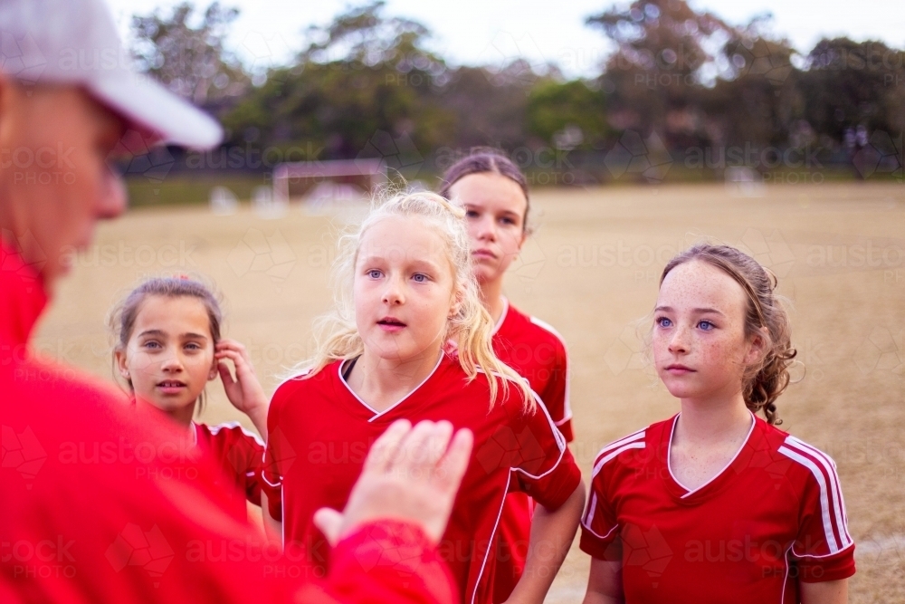 Tween soccer players in a red uniform listening to their coach - Australian Stock Image