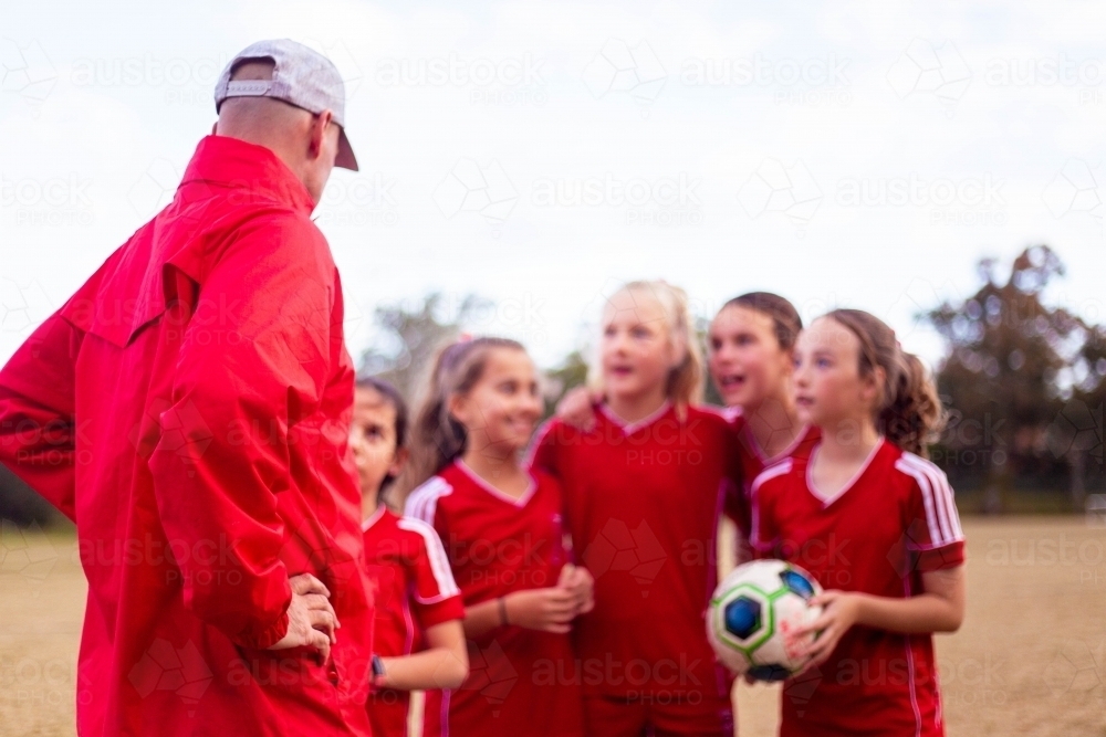 Tween soccer players in a red uniform listening to their coach - Australian Stock Image