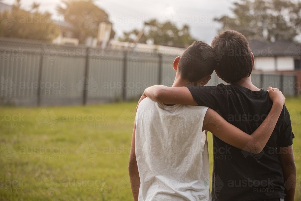 Two aboriginal boys with their arms around one another looking away - Australian Stock Image