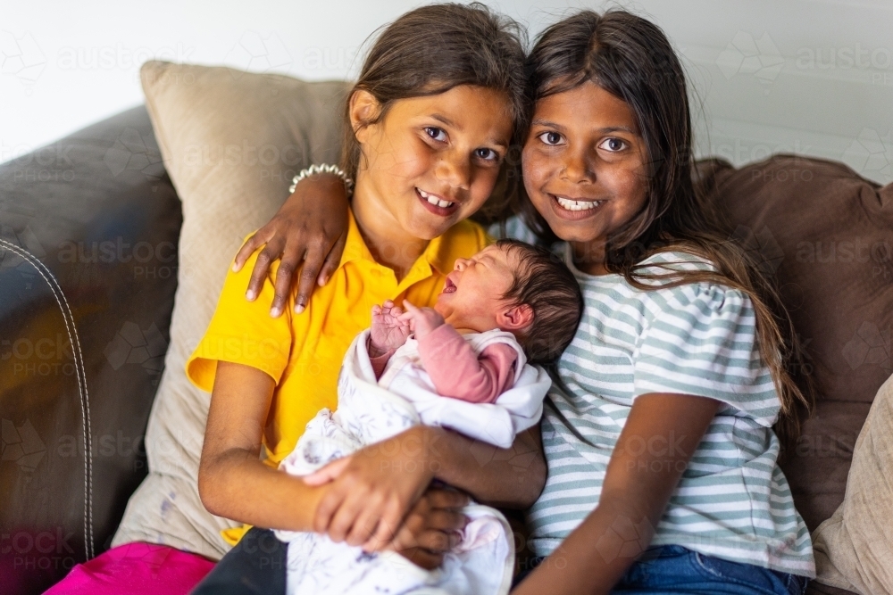 two aboriginal children sitting on sofa holding their newborn baby sister - Australian Stock Image