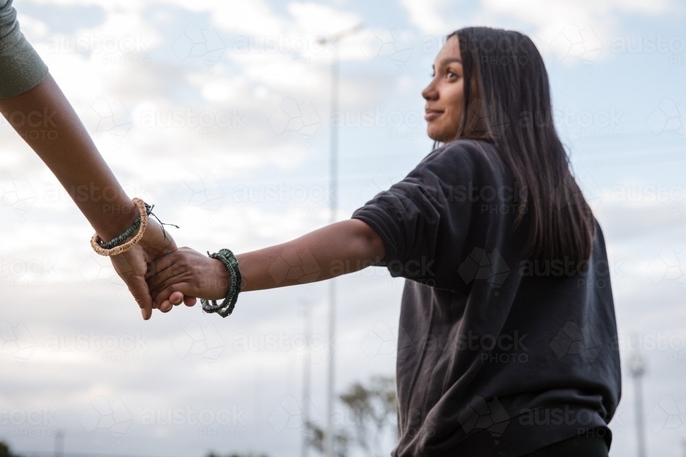 Two Aboriginal girls, outdoors holding hands, wearing traditional woven bracelets - Australian Stock Image