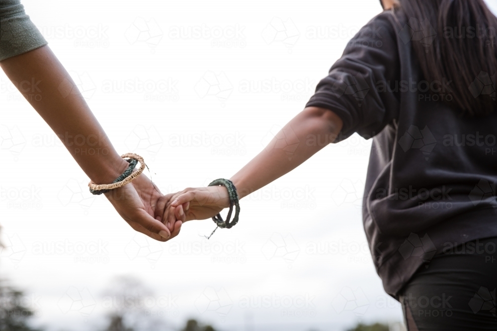 Two Aboriginal girls, outdoors holding hands, wearing traditional woven bracelets - Australian Stock Image