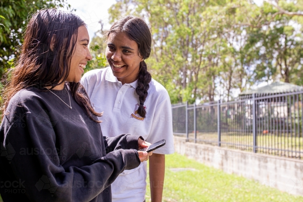 Two Aboriginal girls talking and looking at a phone - Australian Stock Image