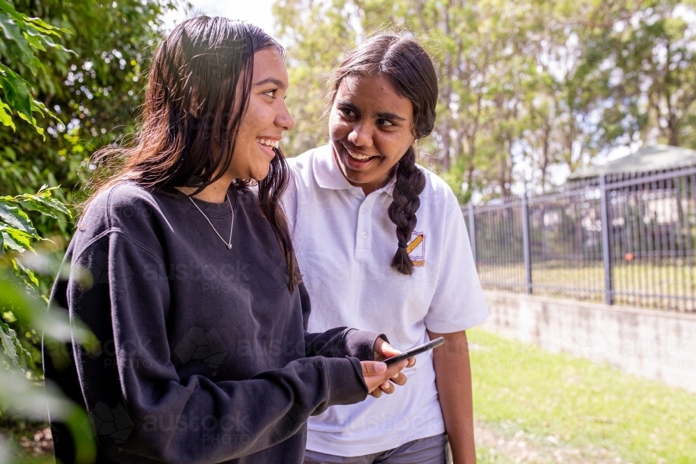 Two Aboriginal girls talking and looking at a phone - Australian Stock Image