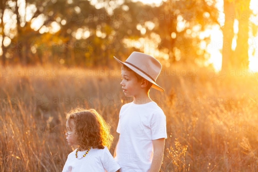 Two aboriginal kids together in grassy paddock in golden sunset light - Australian Stock Image