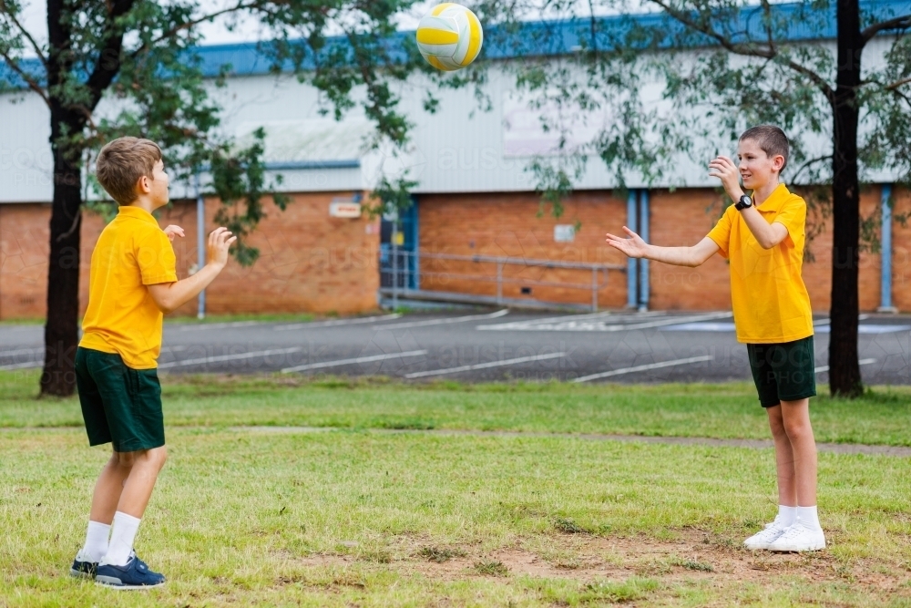 Two Aussie school boys throwing a ball together outside - Australian Stock Image