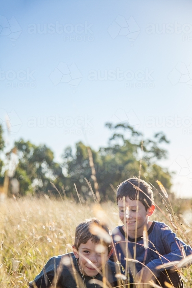 Two boys hiding in grass in a paddock - Australian Stock Image