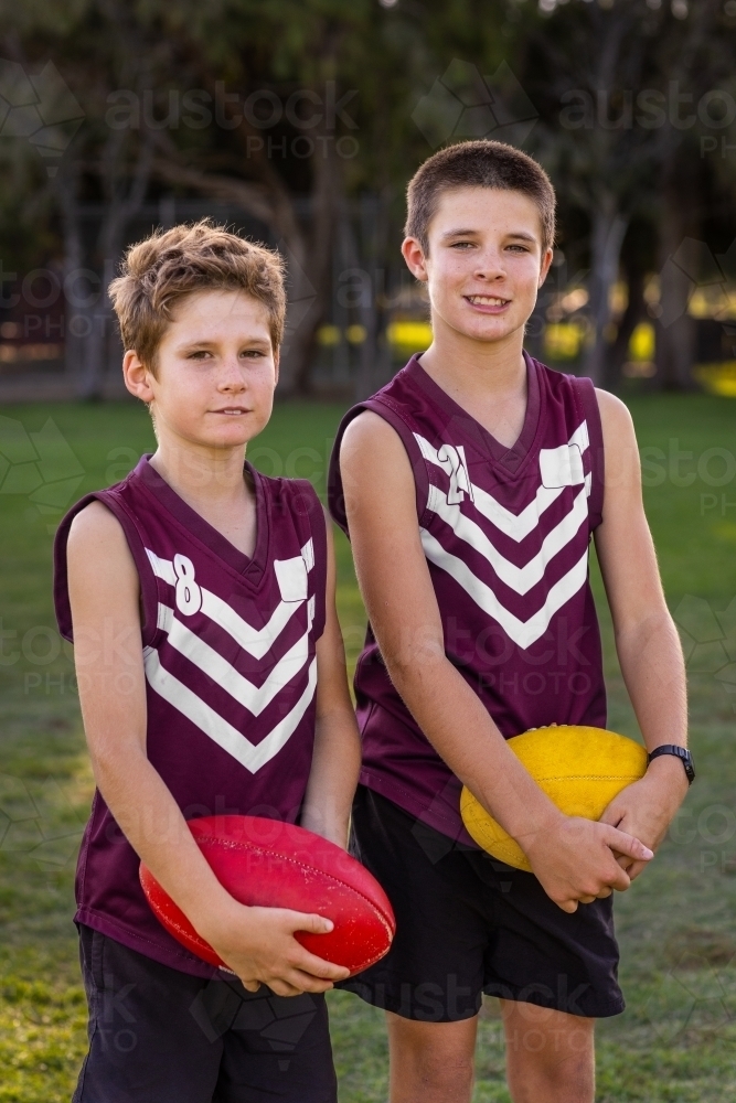 two boys in football uniform holding footballs - Australian Stock Image