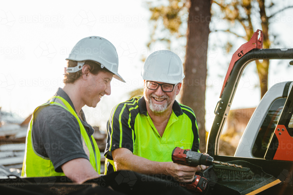 Two builders standing next to ute on construction site one man holding a drill - Australian Stock Image