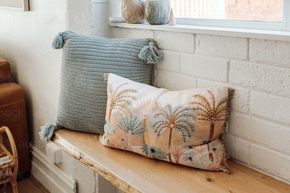 Two decorative pillows on a wooden bench against the brick wall. - Australian Stock Image