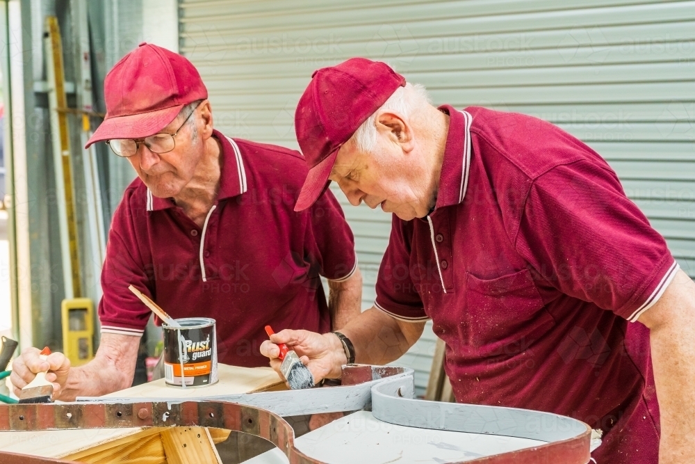 Two elderly handymen painting ironwork together in a Men's shed - Australian Stock Image