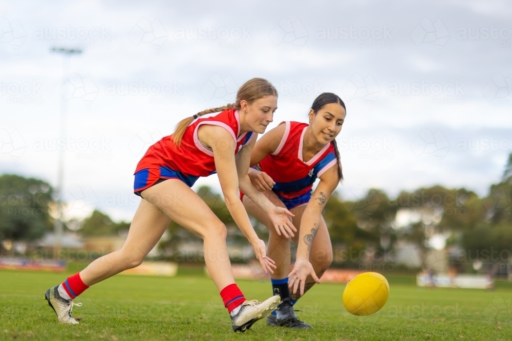 two female football players bending and reaching for ball - Australian Stock Image