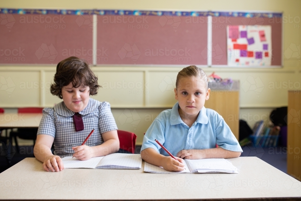 Two girl students writing in a primary school classroom - Australian Stock Image