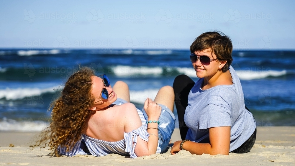 Two girls looking at camera sitting on beach - Australian Stock Image