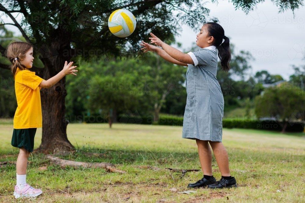 Two girls playing outside at school throwing and catching a ball - Australian Stock Image