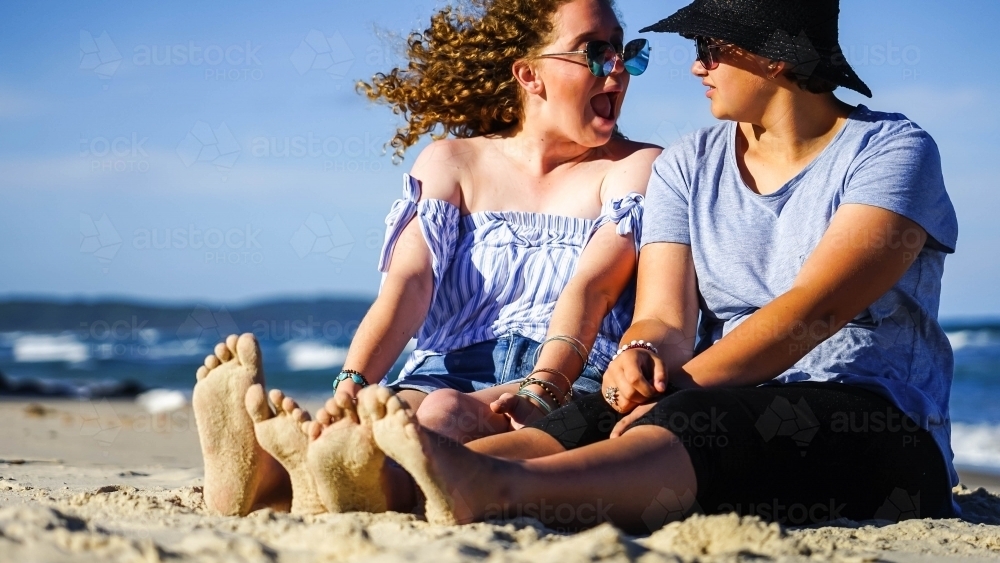 Two girls sitting on beach with sandy feet - Australian Stock Image