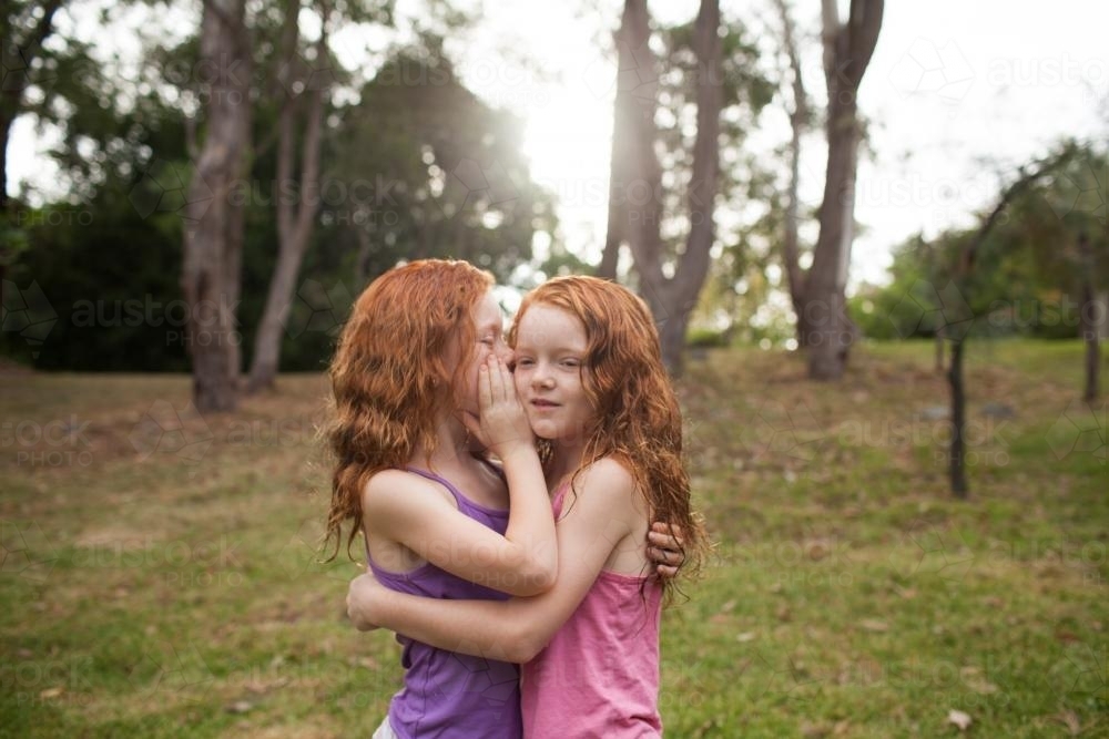 Two girls telling secrets in a field - Australian Stock Image