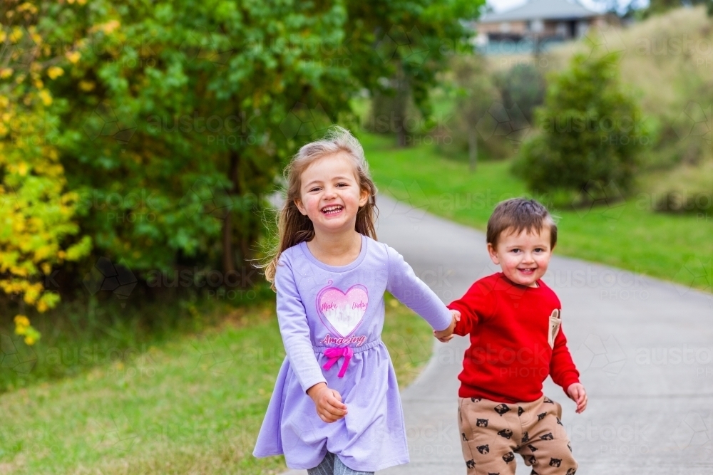 Two happy children running together along a footpath outside - Australian Stock Image