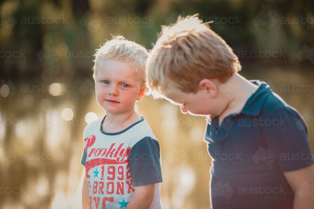 Two little boys exploring near river on an afternoon adventure in the Australian bush - Australian Stock Image