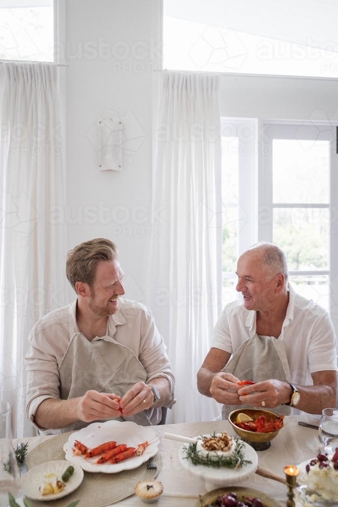 Two men deveining prawns at dinner table - Australian Stock Image