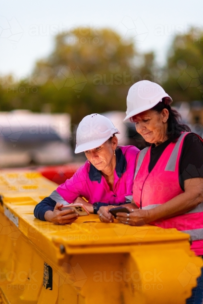 two middle-aged women having a break on a worksite wearing hi-vis and hard hats - Australian Stock Image