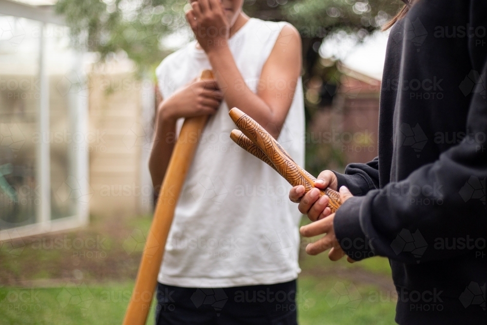 Two people holding Aboriginal instruments in backyard - Australian Stock Image