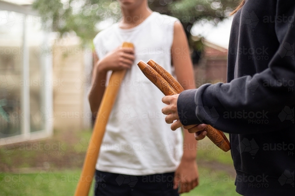 Two people holding Aboriginal instruments in backyard - Australian Stock Image