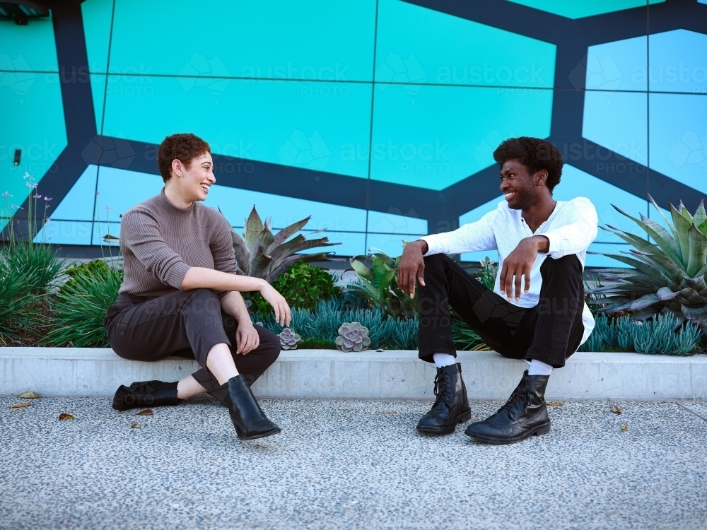 two people smiling at each other while sitting on the sidewalk - Australian Stock Image