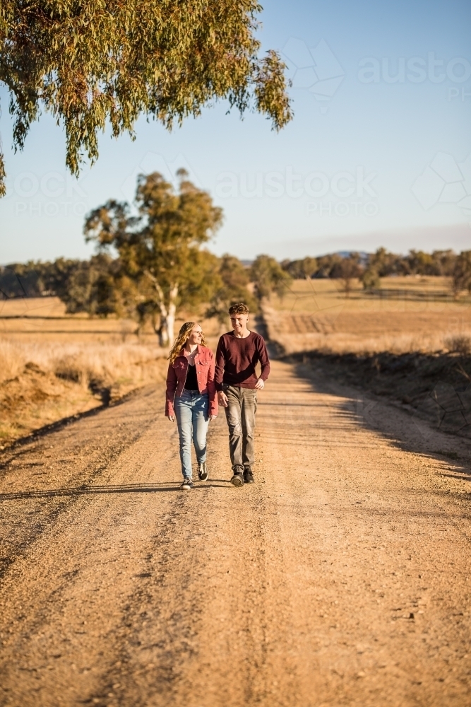 Two people walking down dirt road in afternoon - Australian Stock Image