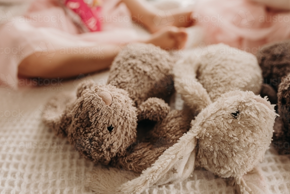 Two plush bunnies on a bed with a child on a pink dress. - Australian Stock Image